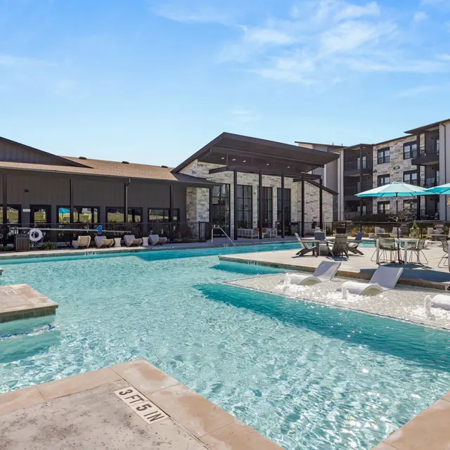A spacious apartment complex pool area with a clear blue sky and lounge chairs.