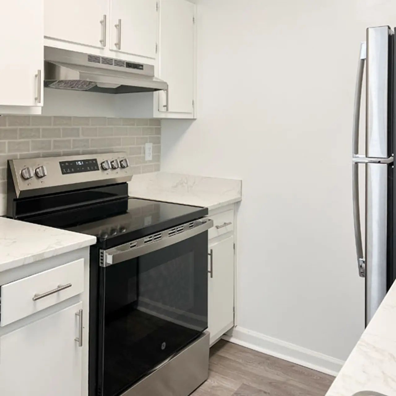 A modern kitchen featuring white cabinetry, stainless steel appliances, and a grey tile backsplash.