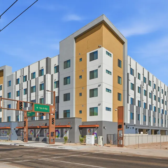 Modern Multi-Story Apartment Building A modern multi-story apartment building with a mix of beige and gray colors, situated at a street intersection with traffic signals and a green directional sign.