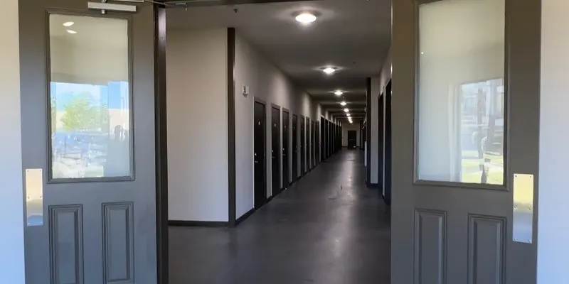 Open double doors leading to a long hallway with multiple doors on either side.