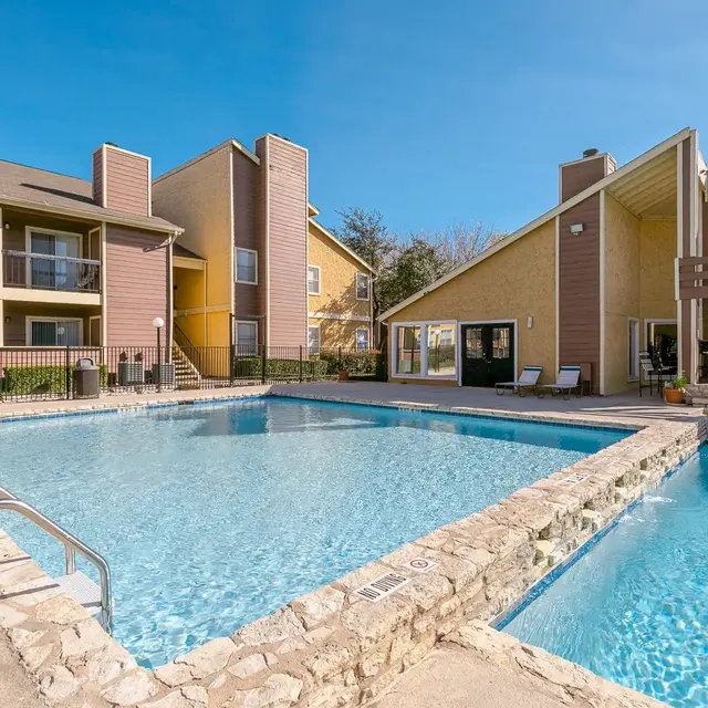 A bright, sunny view of a pool area at an apartment complex, with two distinct swimming pools and surrounding buildings.