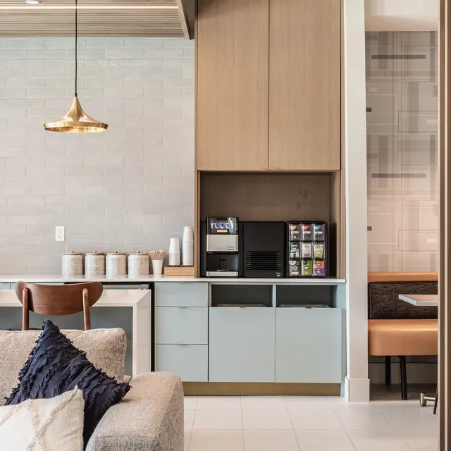 A modern kitchen area featuring a combination of wooden and light-colored cabinetry, a coffee machine, and a cozy seating area with plush cushions.