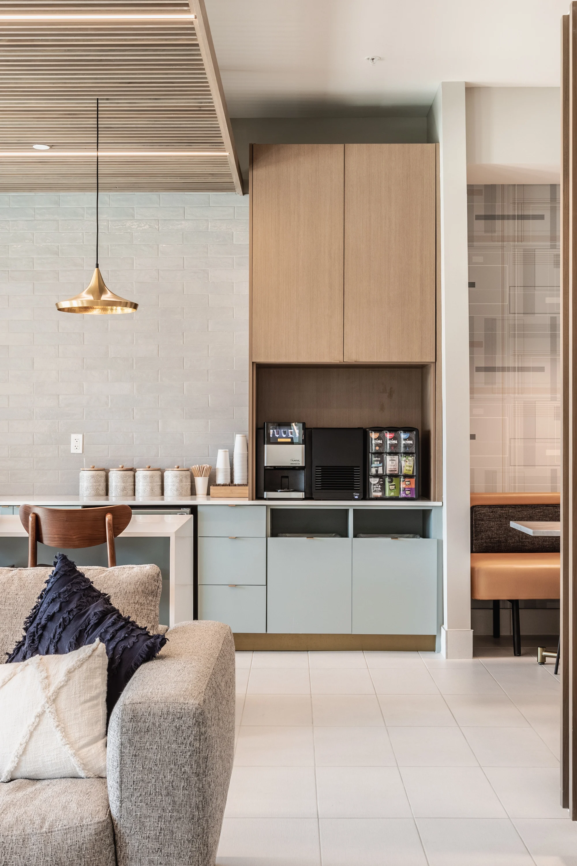 Contemporary Kitchen Space A modern kitchen area featuring a combination of wooden and light-colored cabinetry, a coffee machine, and a cozy seating area with plush cushions.