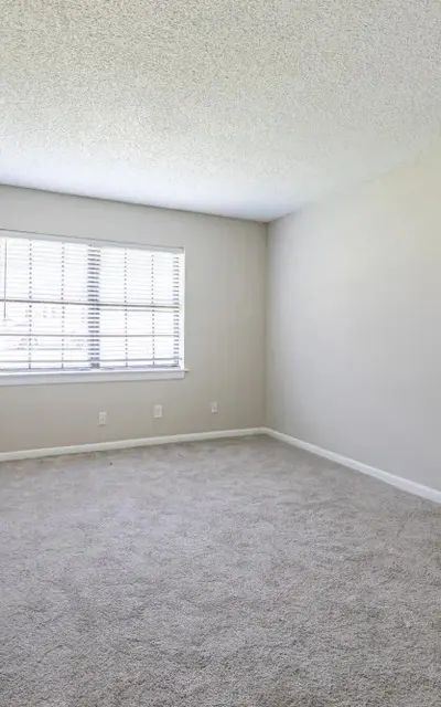 An empty room with light beige walls and carpet. It features a window with multiple panes and a white door leading to another space.