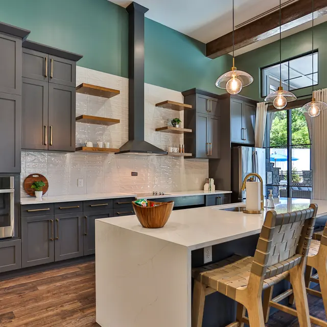 A stylish modern kitchen featuring dark cabinetry, open shelving, and a large island with seating. Large windows allow natural light to fill the space.