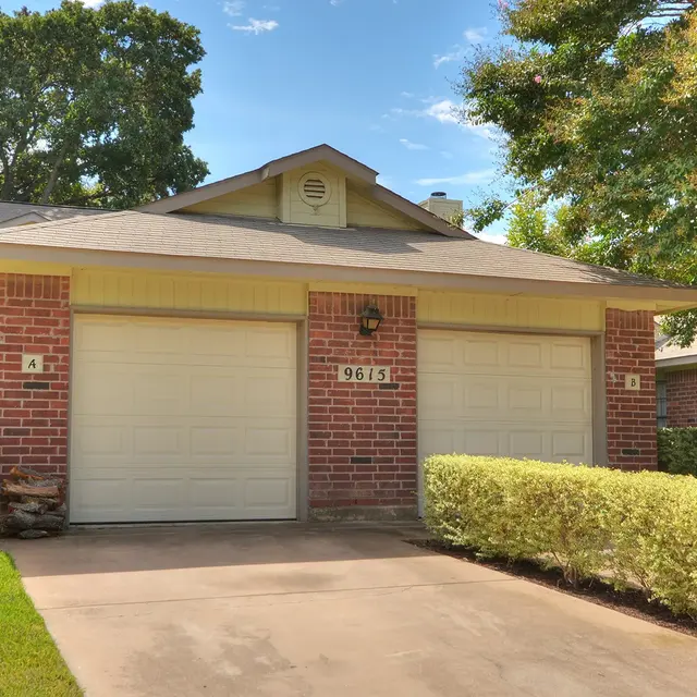 Exterior view of a single-story brick house with a two-car garage and well-maintained landscaping.