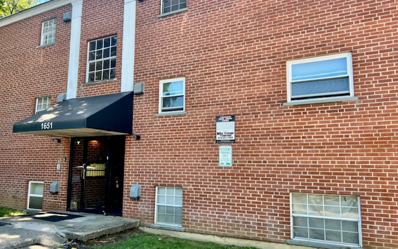 Exterior view of a brick apartment building with an entrance awning and multiple windows.