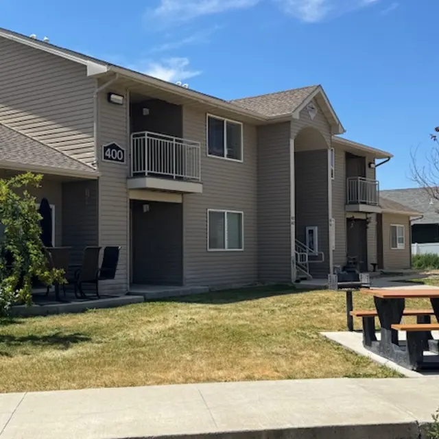 View of an apartment complex featuring beige exterior, balconies, and landscaped yard on a sunny day.