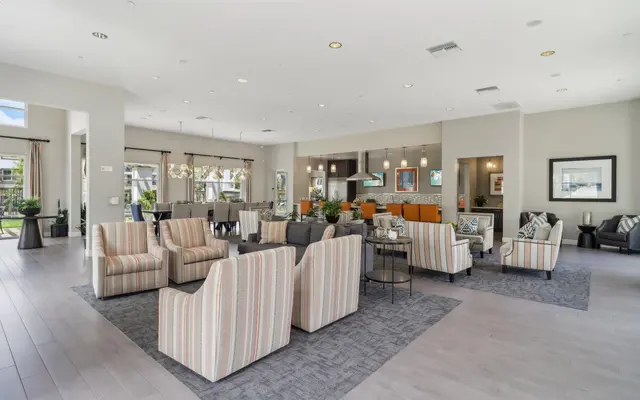 A modern lounge area featuring multiple seating arrangements, with striped and solid-colored chairs and tables, large windows allowing natural light, and a cozy atmosphere.