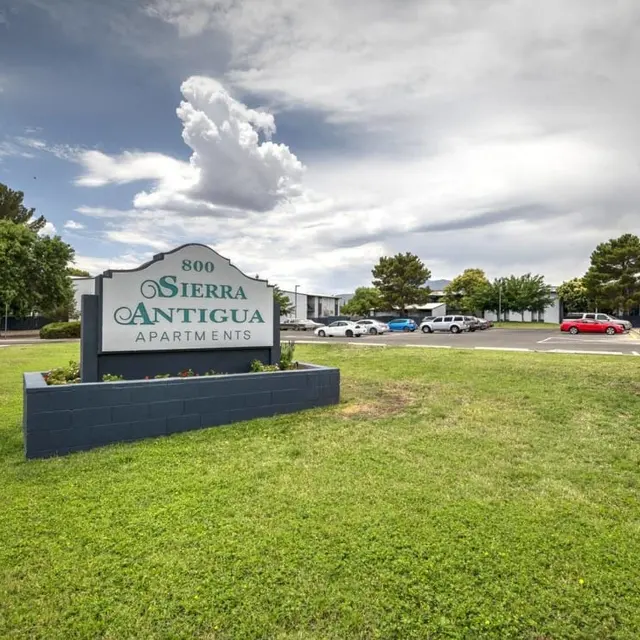 Sign for Sierra Antigua Apartments with a grassy area and cars parked in the background.