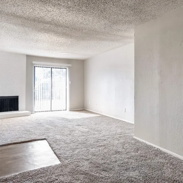 A spacious living room with carpeted flooring, a fireplace, and sliding glass doors leading to an outdoor area.