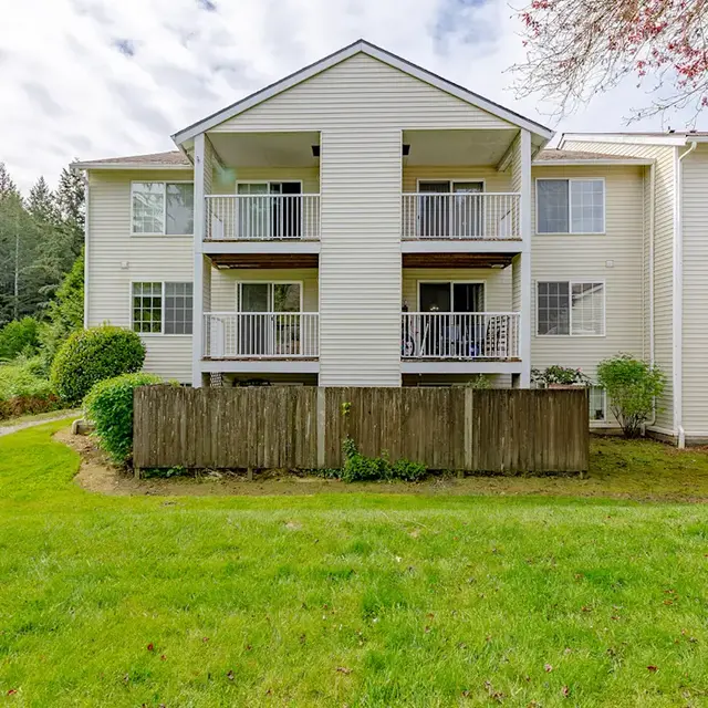 Exterior view of a two-story apartment building with balconies and lush greenery surrounding it.