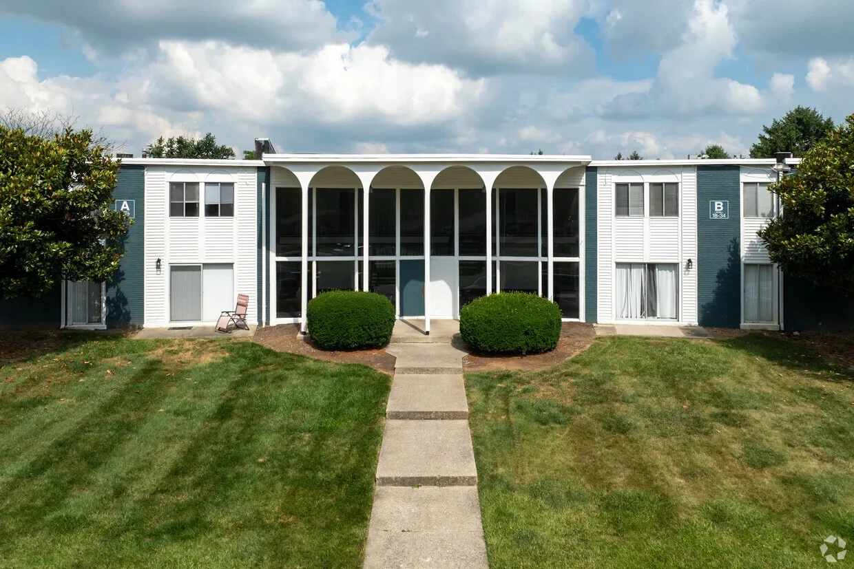 Apartment Complex Front View Front view of an apartment complex with two symmetrical sections labeled A and B, featuring a walkway, green shrubs, and blue sky with clouds.