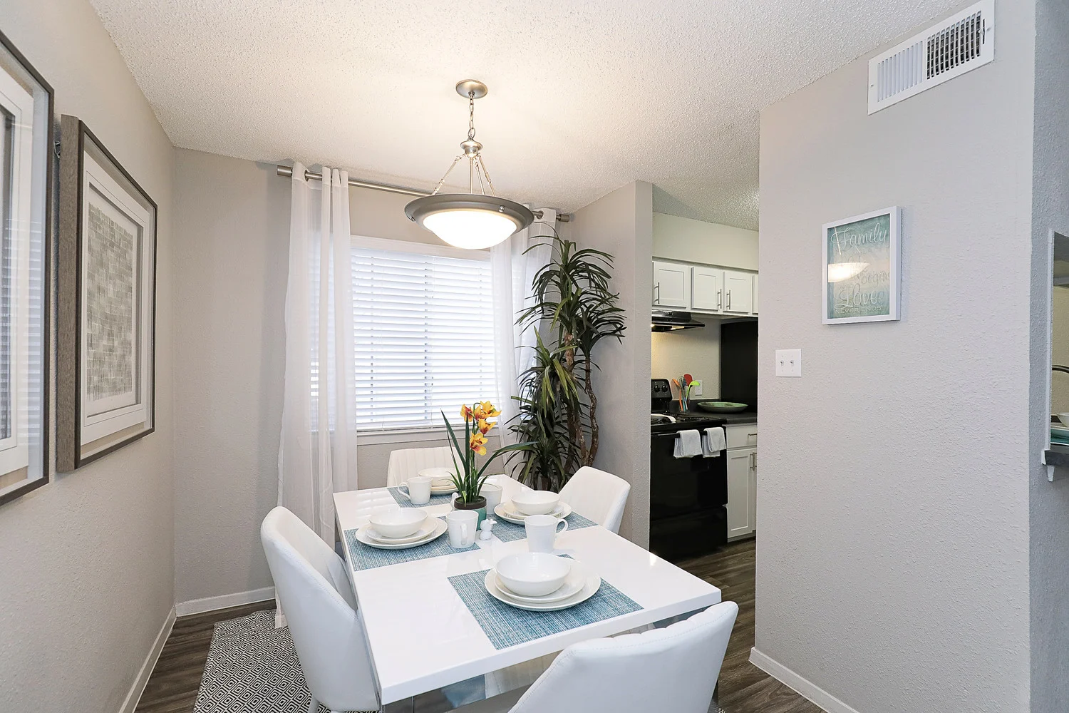 City Crest Apartments - Modern dining area with a white table set for four, surrounded by bright walls and a small kitchen visible in the background.