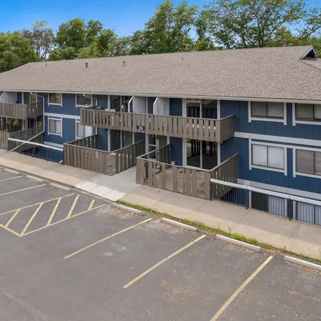 A blue two-story apartment building with multiple balconies overlooking an empty parking lot.