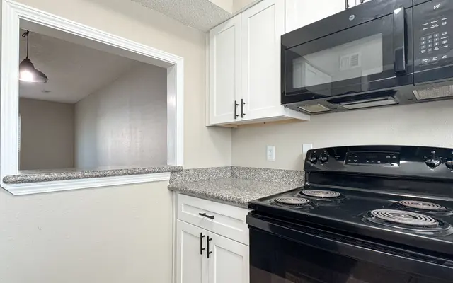 A modern kitchen featuring white cabinets, a black stove, and a microwave. There's a countertop with a view to another room through an open pass-through.