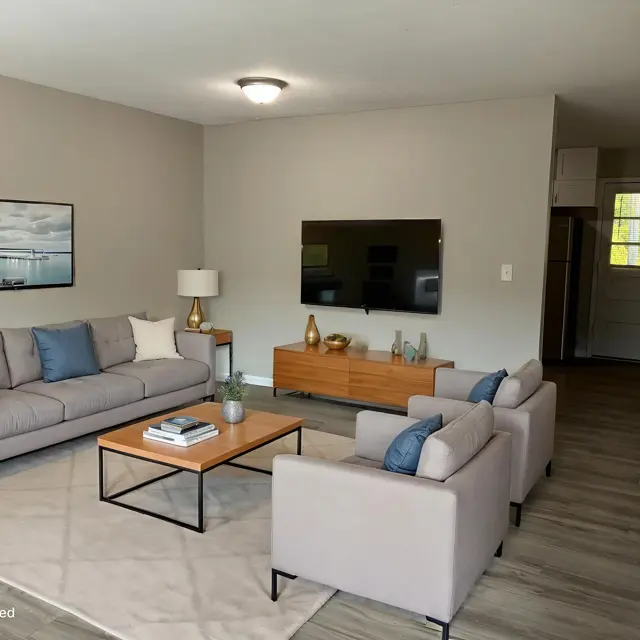 Stylish Living Room Setup A modern living room featuring two light gray sofas, a wooden coffee table, and a TV stand with a large screen TV. The room has neutral walls and wood flooring, with natural light coming in from a door at the back.