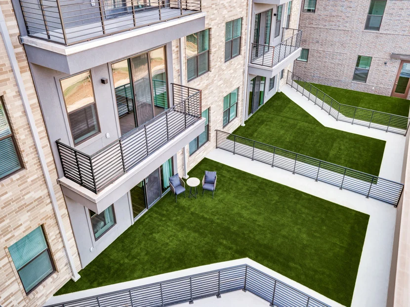 Modern Apartment Courtyard Design A view of a modern apartment courtyard featuring well-maintained artificial grass, balconies, and seating areas.
