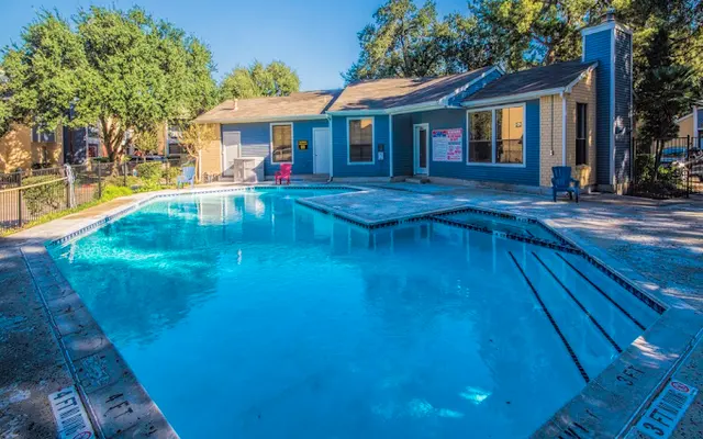 A clear blue swimming pool surrounded by a pathway and lounge chairs, with a residential building in the background.
