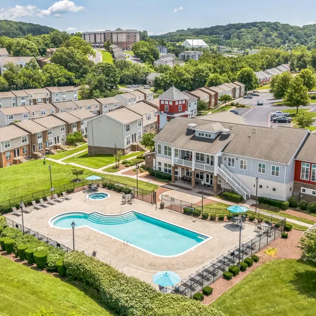 Aerial View of Apartment Complex with Pool Aerial view of a residential apartment complex featuring a swimming pool, landscaped green spaces, and parked cars.