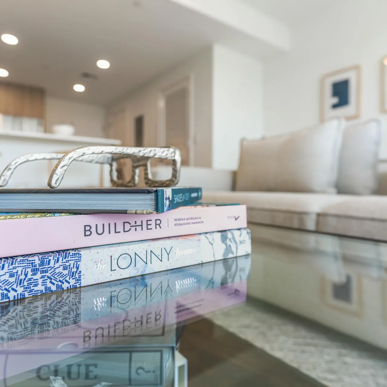 Stack of design and lifestyle books on a glass coffee table in a bright, modern living room.
