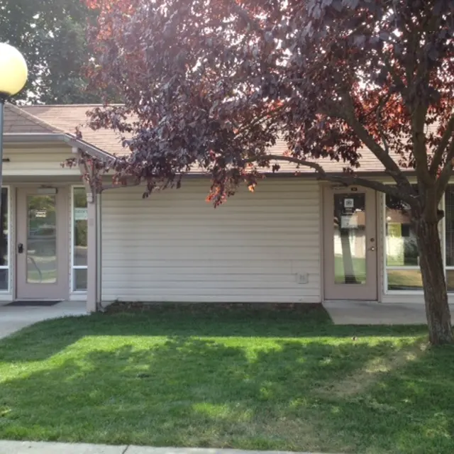 Residential Building Exterior Exterior view of a single-story residential building surrounded by grass and a tree with maroon leaves, featuring a pathway and a lamp post.