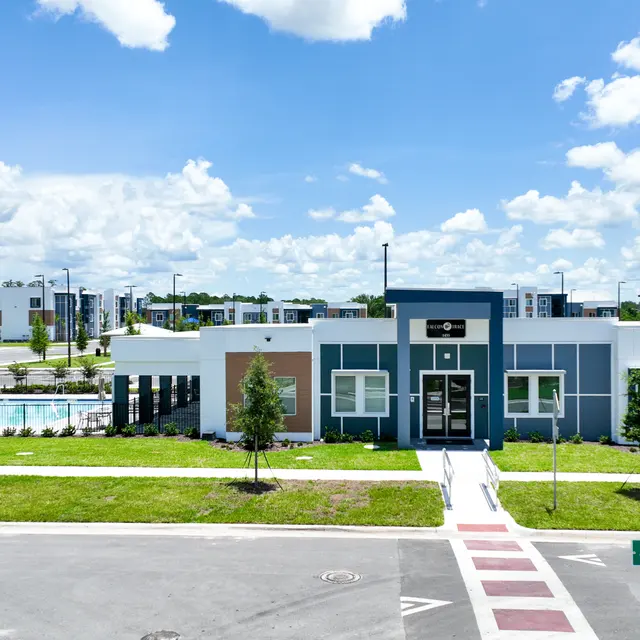 A modern apartment complex with a pool in the background under a blue sky with fluffy clouds.