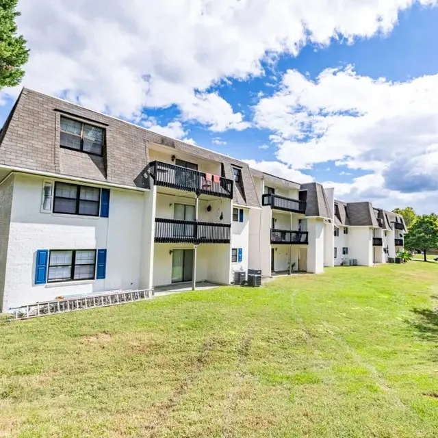 Exterior view of a multi-story apartment complex with a lawn and trees.