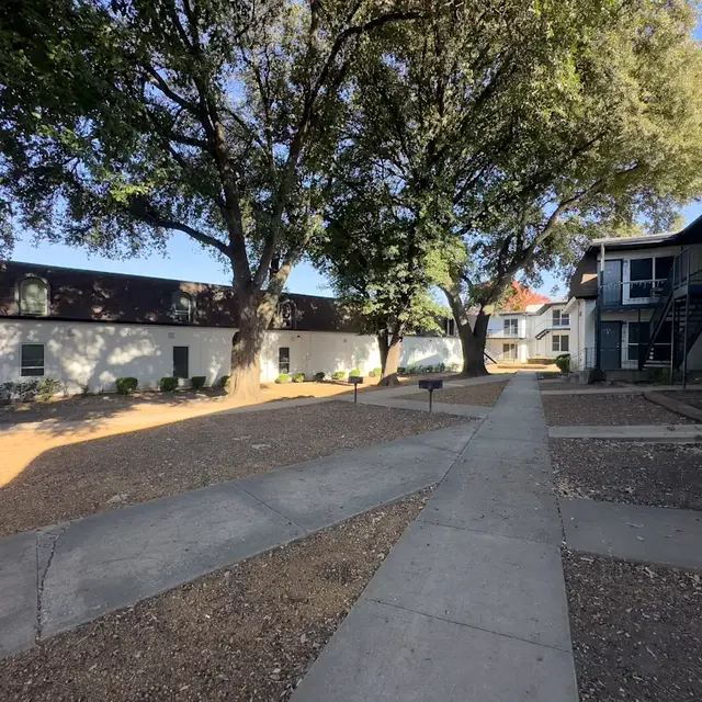 A peaceful courtyard in an apartment complex featuring walking paths, trees, and buildings.