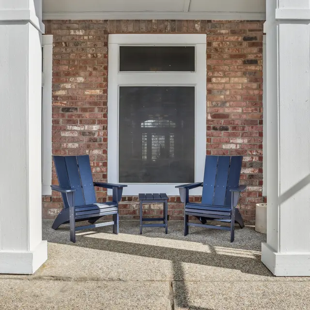 An outdoor seating area featuring two blue chairs and a small table, surrounded by brick walls and white columns.