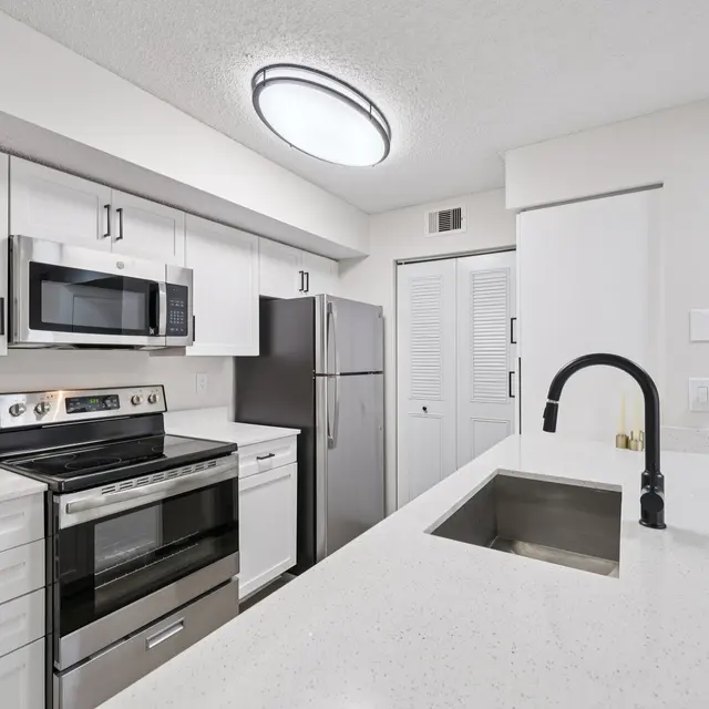 A modern kitchen showcasing white cabinets, stainless steel appliances, and a spacious countertop with a sink. The kitchen has a sleek design with a bright ceiling light and an organized layout.