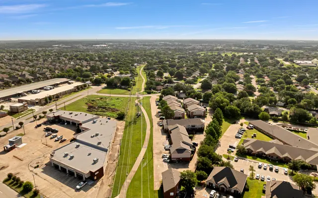 Aerial view of a suburban area showing residential homes, green spaces, and a pathway.