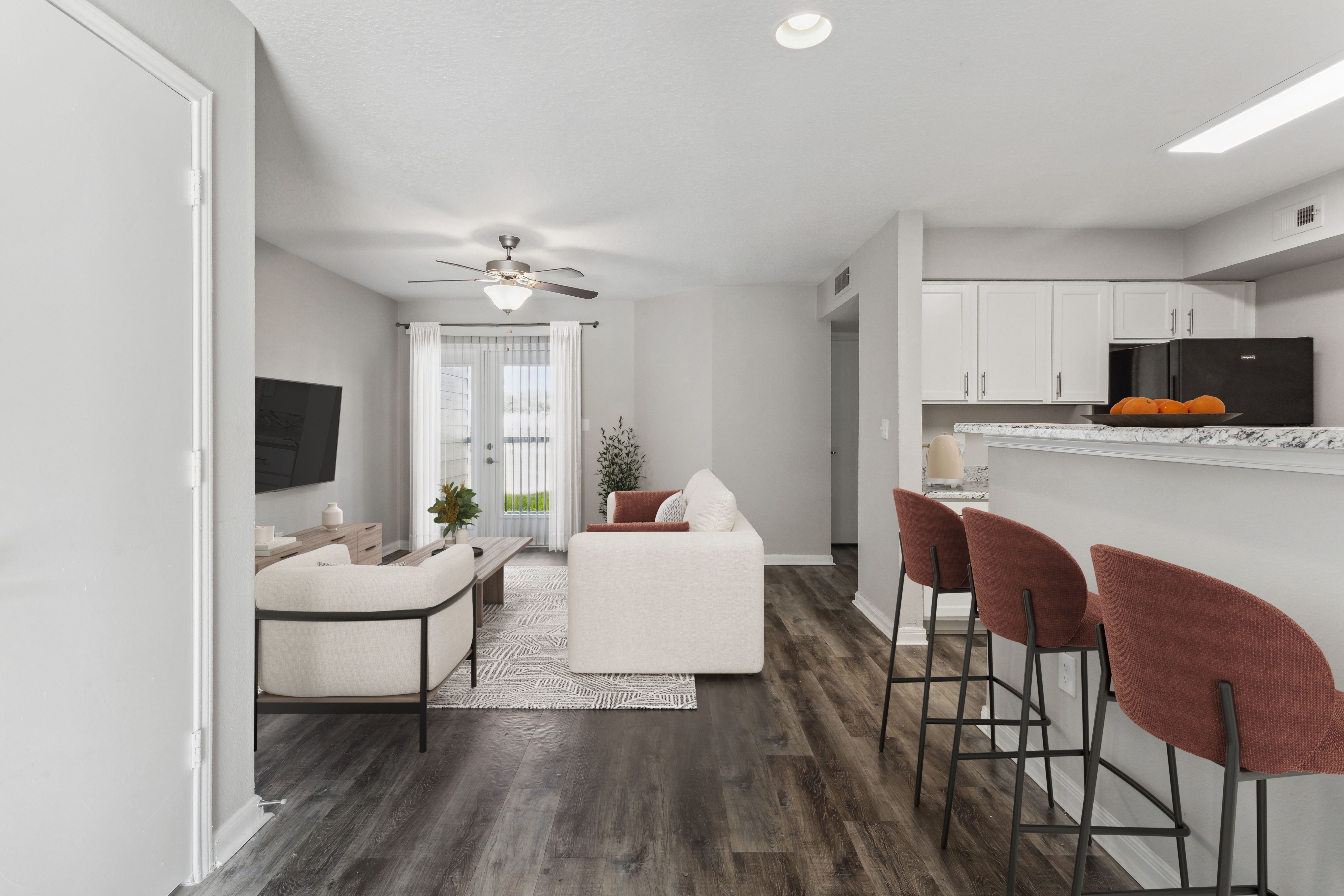 Contemporary living room and kitchen space featuring a white sofa, decorative plants, and a bar with high stools.