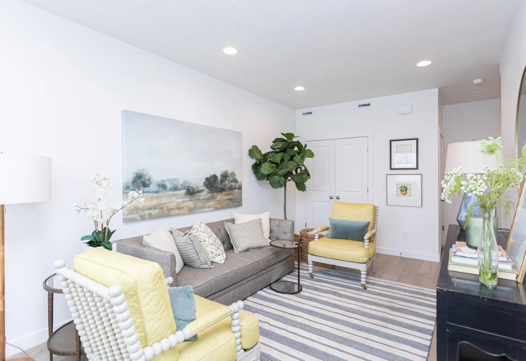 Modern Living Room Design A cozy modern living room featuring two yellow chairs, a gray sofa with decorative pillows, a large painting on the wall, a potted plant, and a striped rug.