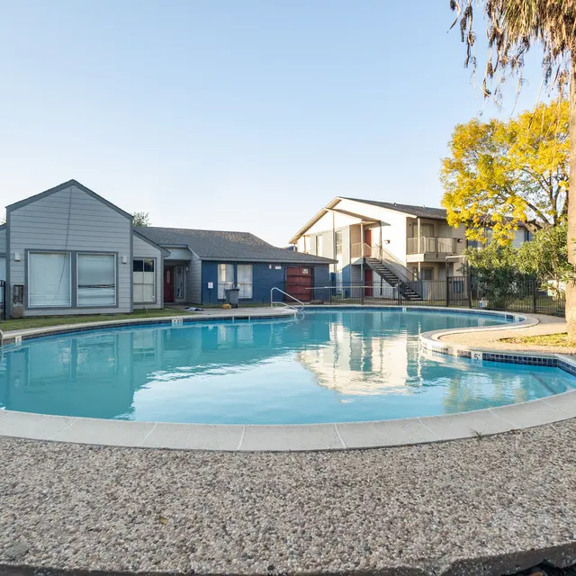 A tranquil swimming pool area surrounded by residential buildings, featuring a circular pool and lush greenery.