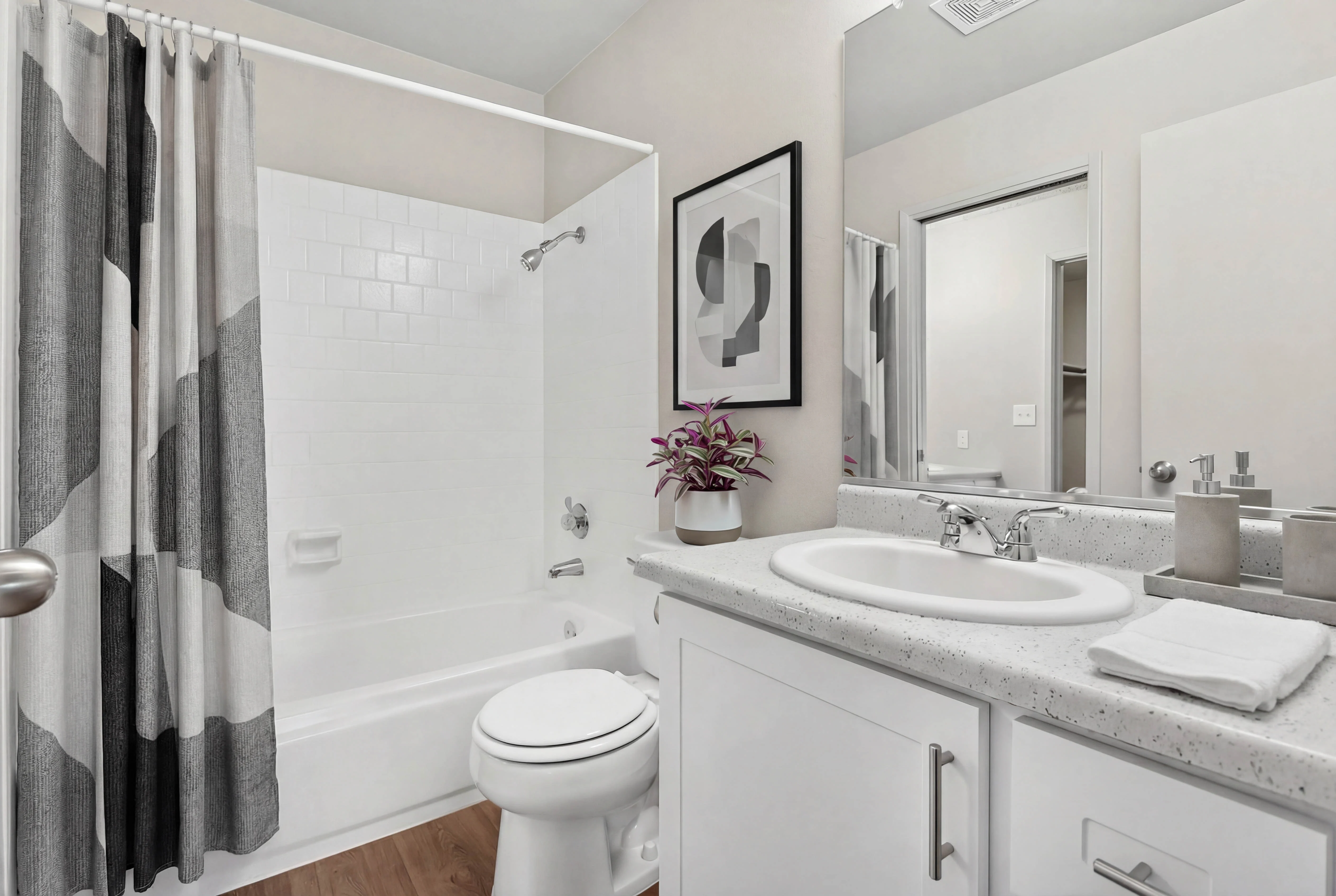 A modern bathroom featuring a bathtub with a shower curtain, a white vanity with a sink, and a small potted plant on the counter.