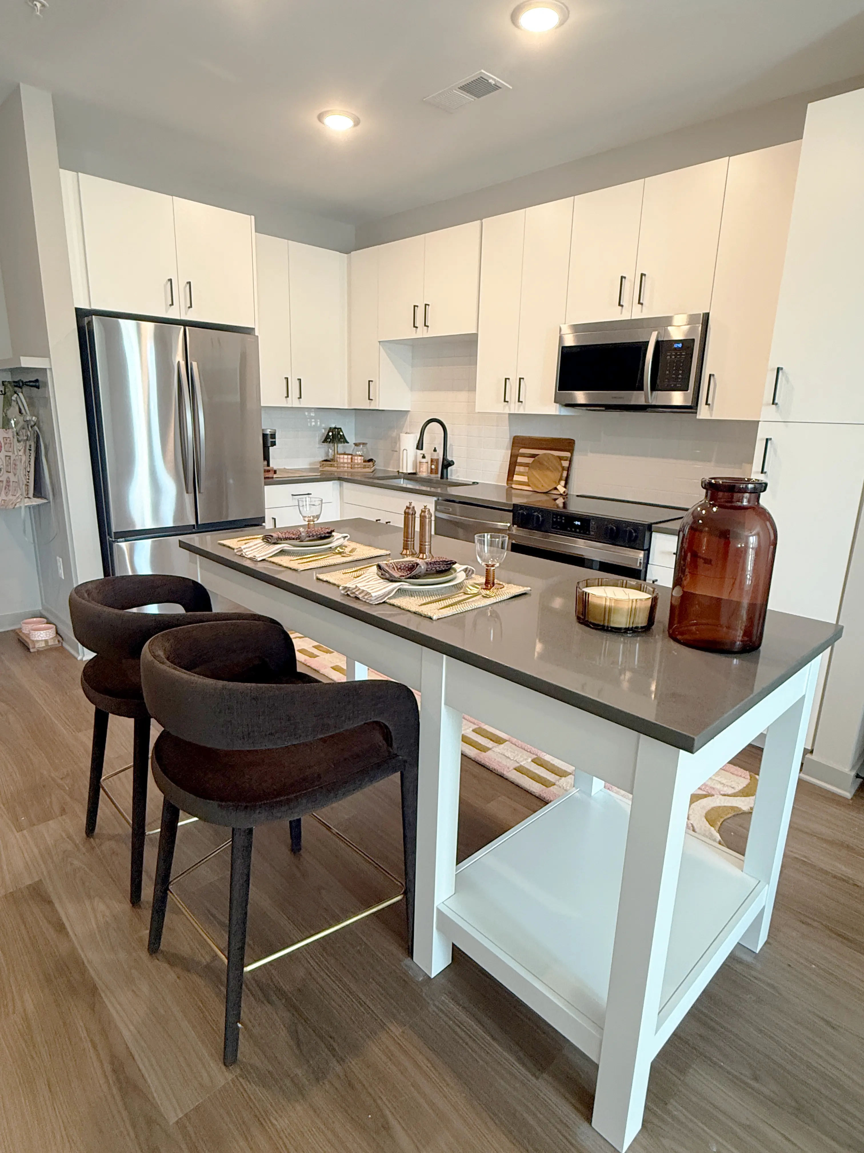 A modern kitchen featuring white cabinets, stainless steel appliances, and a gray countertop with four barstools on one side.