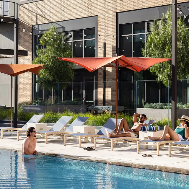 A modern pool area with lounge chairs and umbrellas, featuring people relaxing by the water.