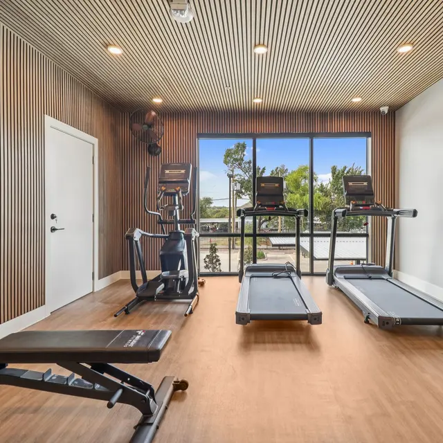 Modern Gym Interior A modern gym interior with exercise equipment, including treadmills and a workout bench, against a backdrop of large windows letting in natural light.
