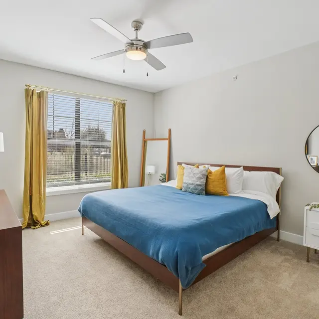 A stylish modern bedroom featuring a blue bedspread, wooden furniture, and large windows with curtains.
