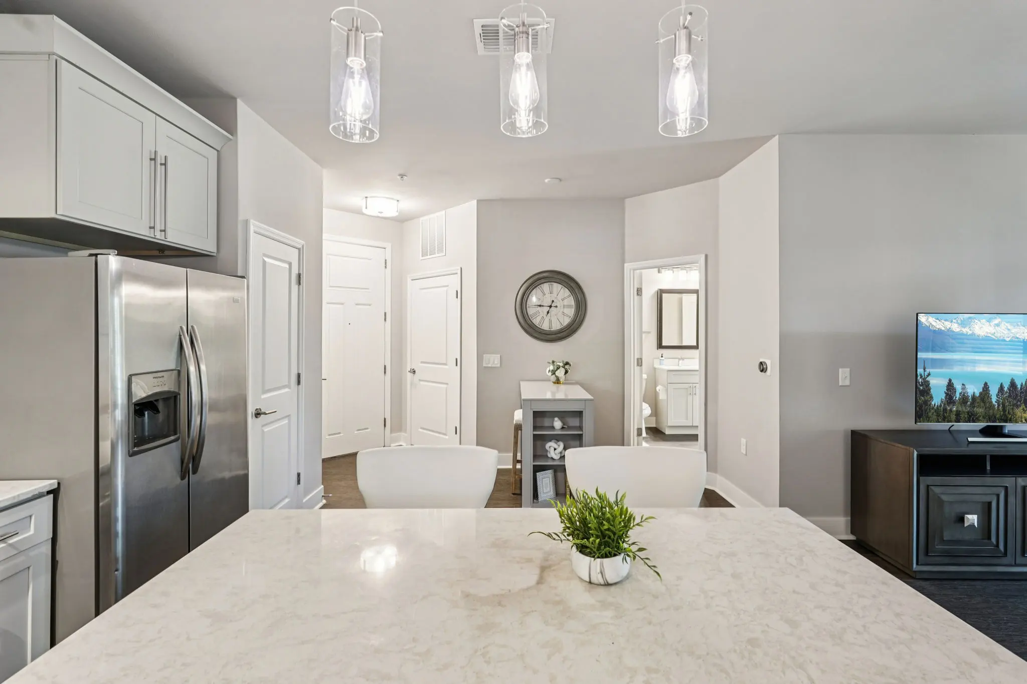 Bright modern kitchen and living area with a large island, stainless steel refrigerator, and a television displaying a scenic image.