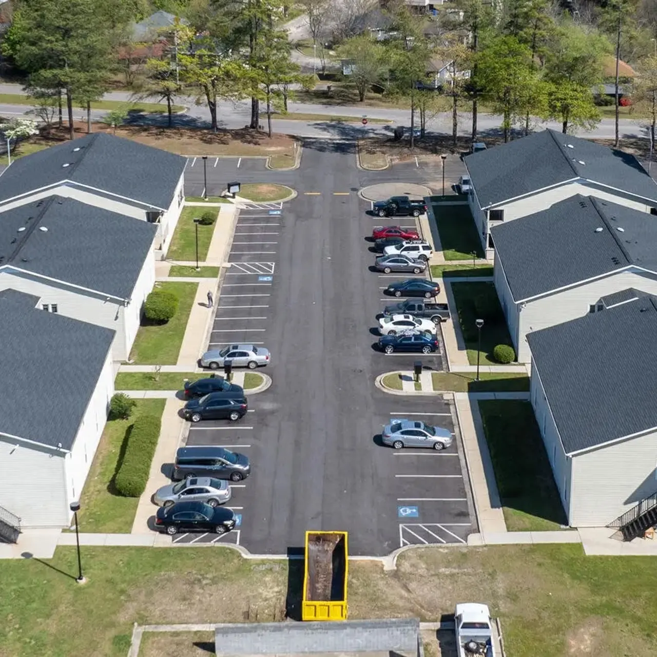 Aerial view of a residential apartment complex featuring multiple buildings, parking areas, and surrounding greenery.