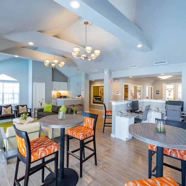 Spacious Modern Living Area A spacious modern living area featuring various seating arrangements and bright decor. The room has a high ceiling with stylish lighting and large windows providing natural light. The furniture includes circular tables with colorful chairs and a cozy seating area.