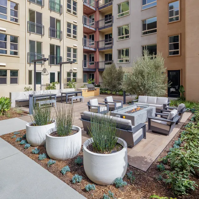 A modern outdoor lounge area with seating and greenery in an apartment complex courtyard.