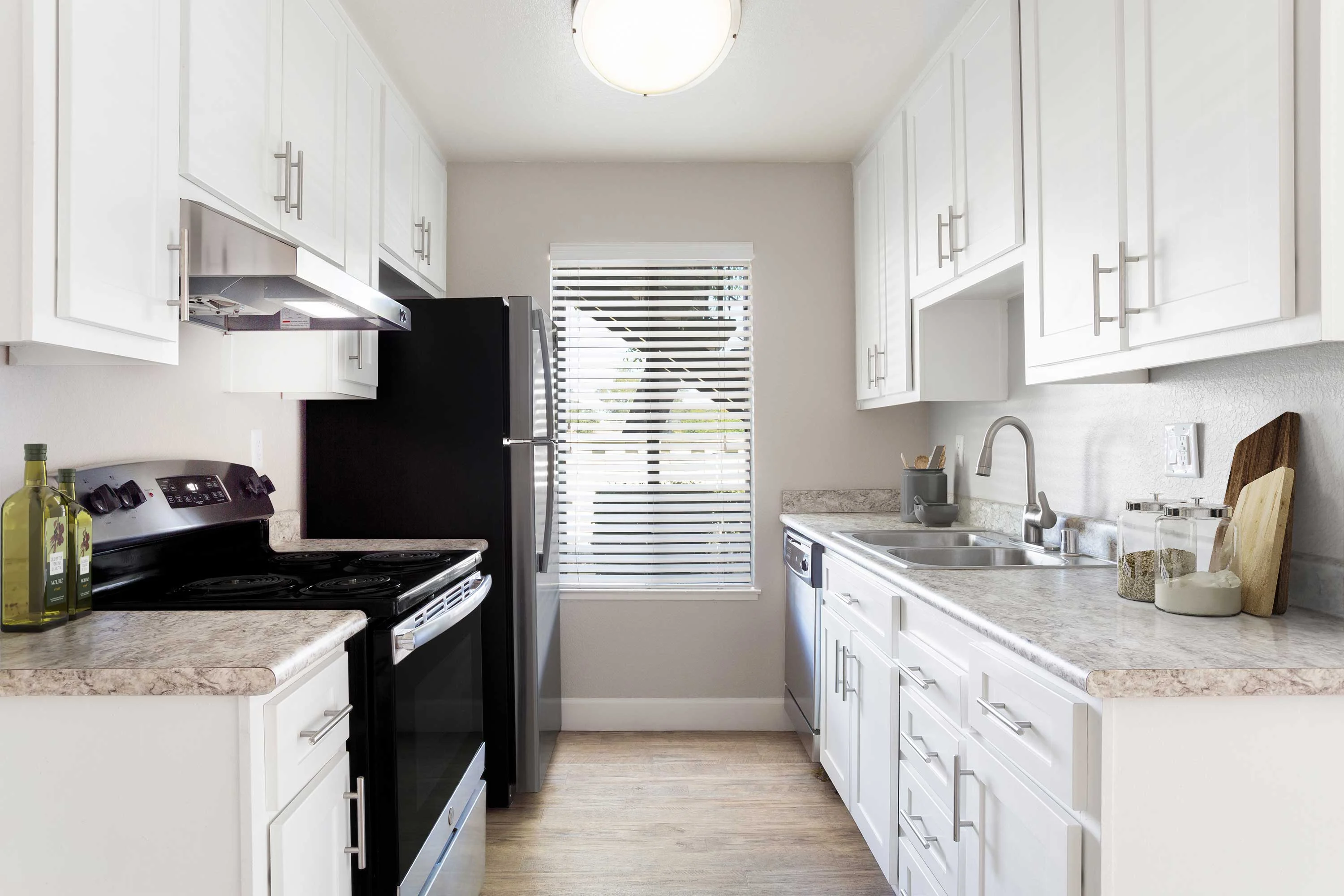 Modern Kitchen Interior A modern kitchen featuring white cabinets, an oven, cooktop, and black refrigerator. There is a window with blinds and a sink with kitchen utensils on the counter.