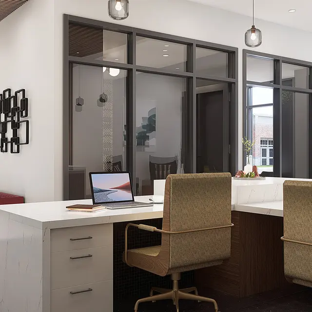 A contemporary office interior featuring a reception desk, two chairs, and large windows allowing natural light. There is a modern light fixture and decorative wall art nearby. A comfortable seating area is visible in the background.