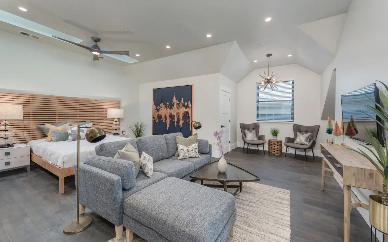 A spacious modern bedroom featuring two beds with a wooden headboard, a cozy lounge area with a sectional sofa, and contemporary decor including art on the walls and stylish lighting.