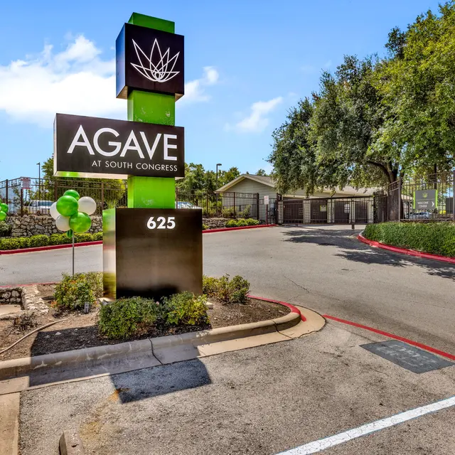 Entrance sign for Agave at South Congress with a green and black color scheme and surrounding landscaping.