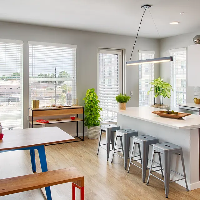 Modern kitchen with white cabinets, a large island, bar stools, and a dining table. Bright windows offer a view outside.
