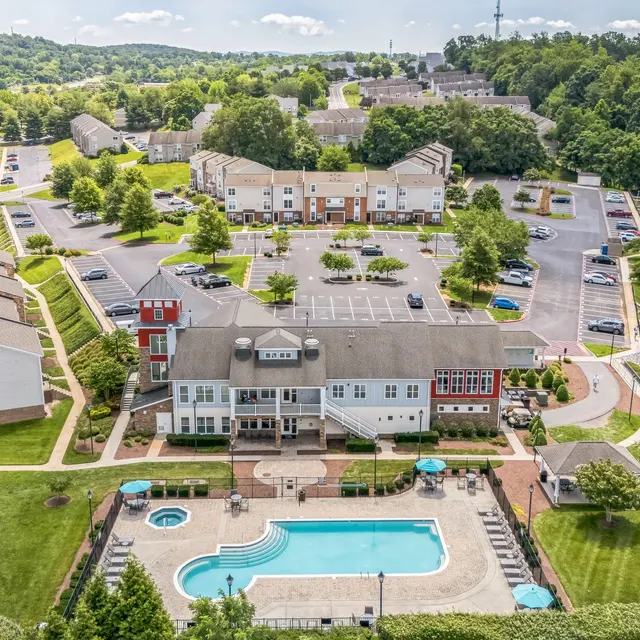 Aerial View of Apartment Complex Aerial view of a residential apartment complex featuring multiple buildings, a swimming pool, green lawns, and parking areas.
